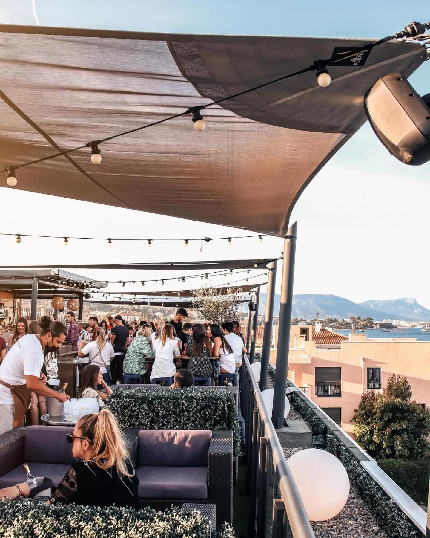 Terrasse ombragée avec des clients assis à des tables et des canapés.