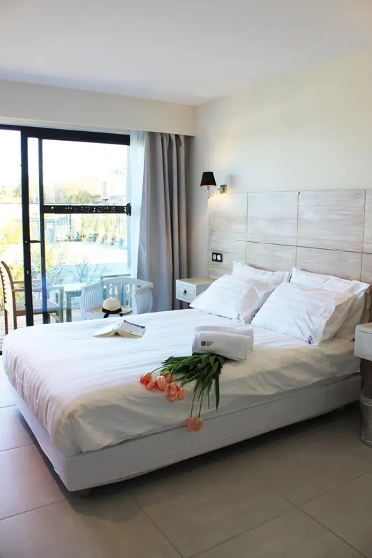 Une chambre lumineuse avec un grand lit recouvert de linge blanc et un bouquet de fleurs.