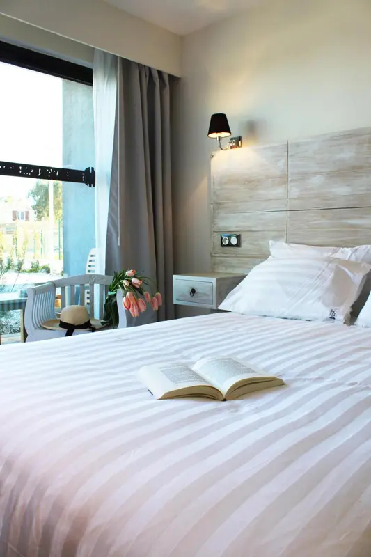 Une chambre lumineuse avec un lit recouvert de draps blancs et un livre ouvert.