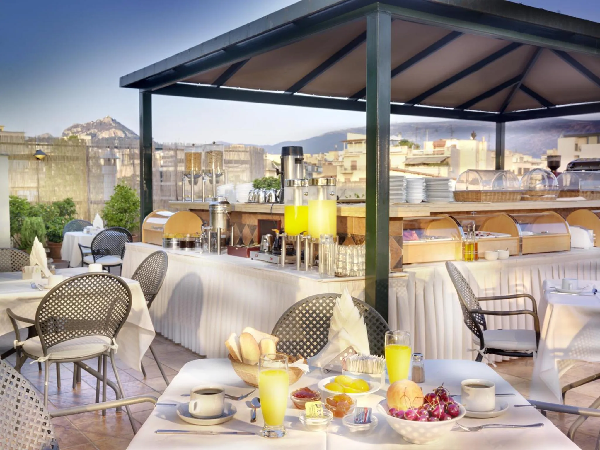 Une table est dressée pour le petit-déjeuner sur une terrasse ombragée avec vue sur la ville.