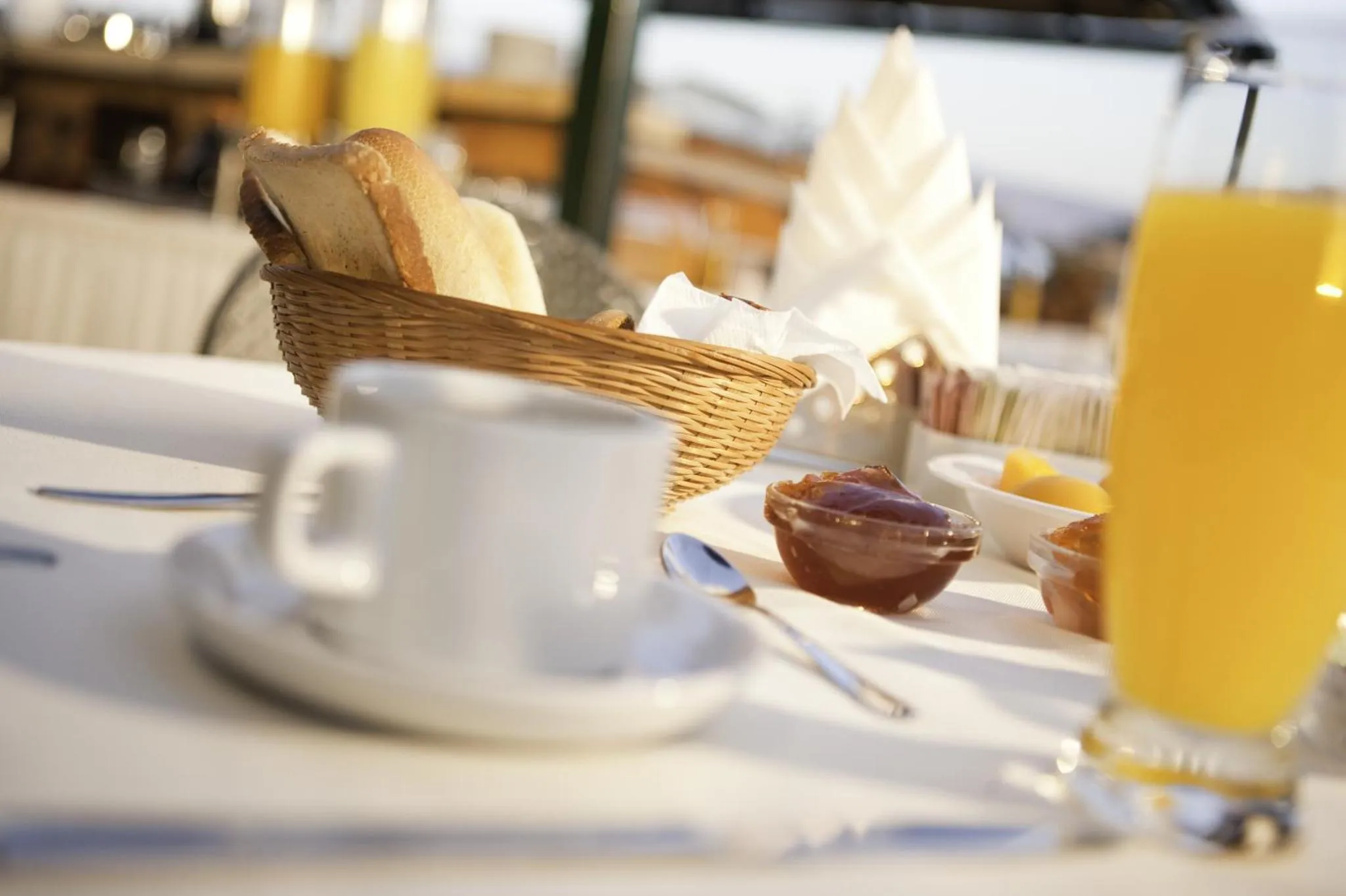 Une table est dressée pour le petit-déjeuner avec du pain, une tasse de café et du jus d'orange.