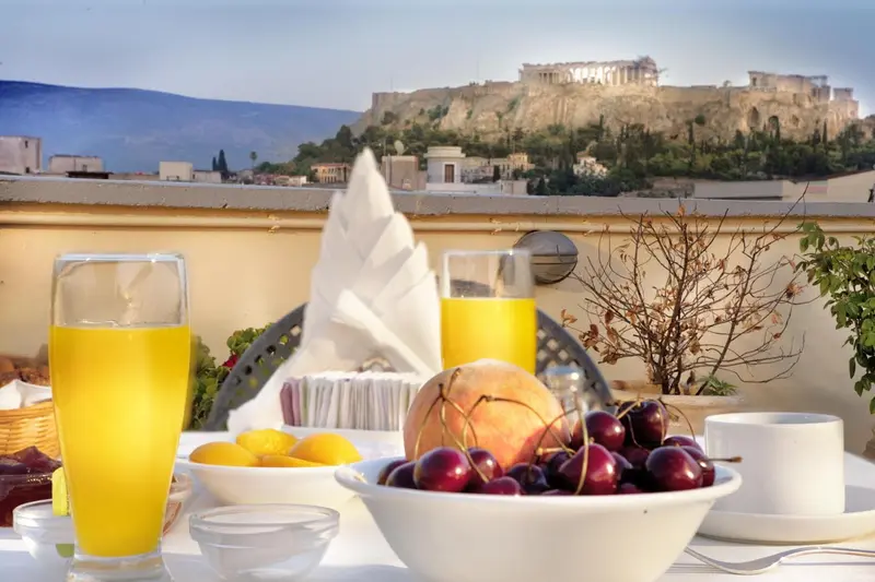 Une table est dressée avec des fruits et des jus de fruits sur une terrasse ensoleillée.