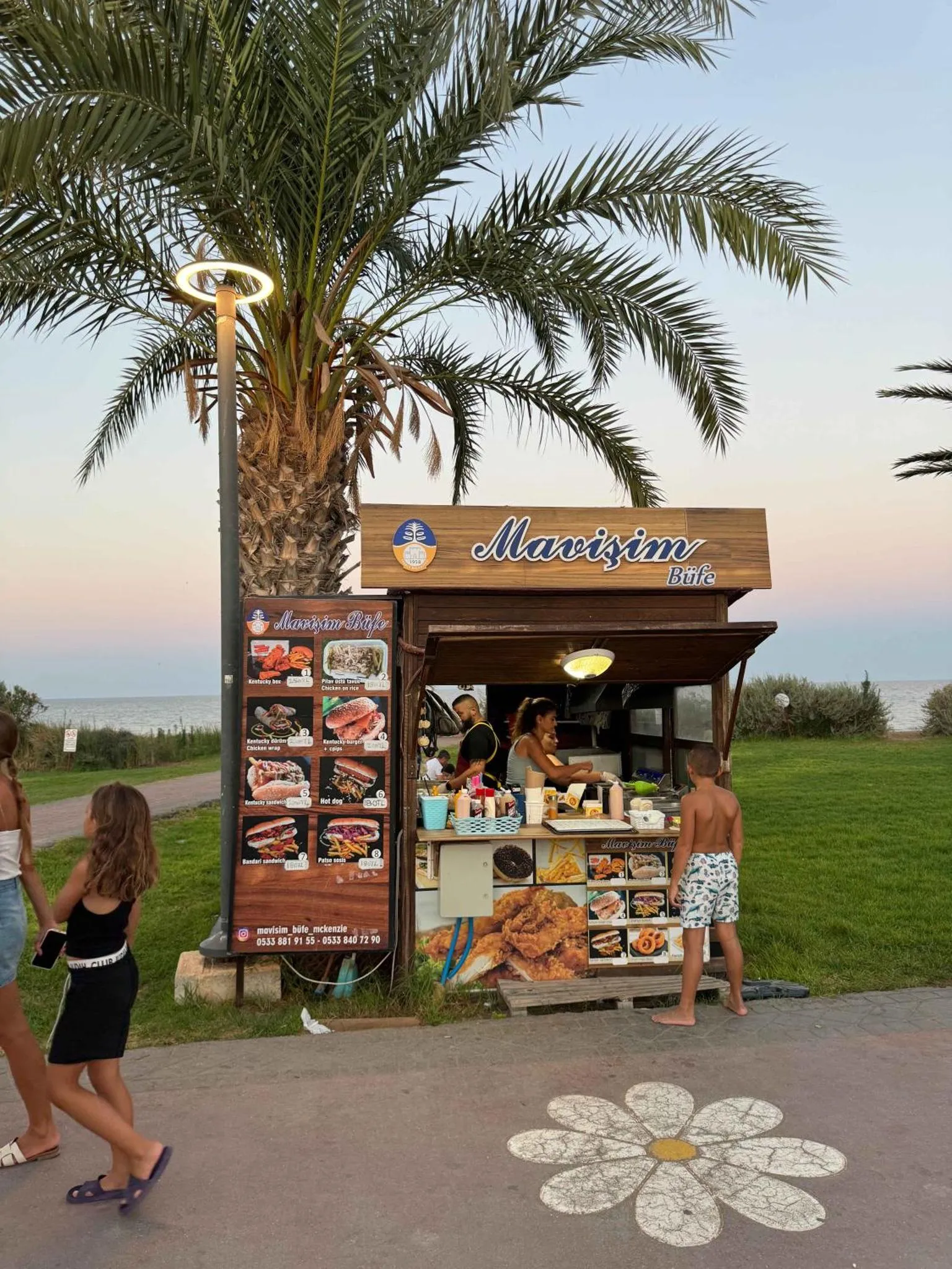 Un kiosque de restauration en bord de mer, avec des passants et une végétation luxuriante.