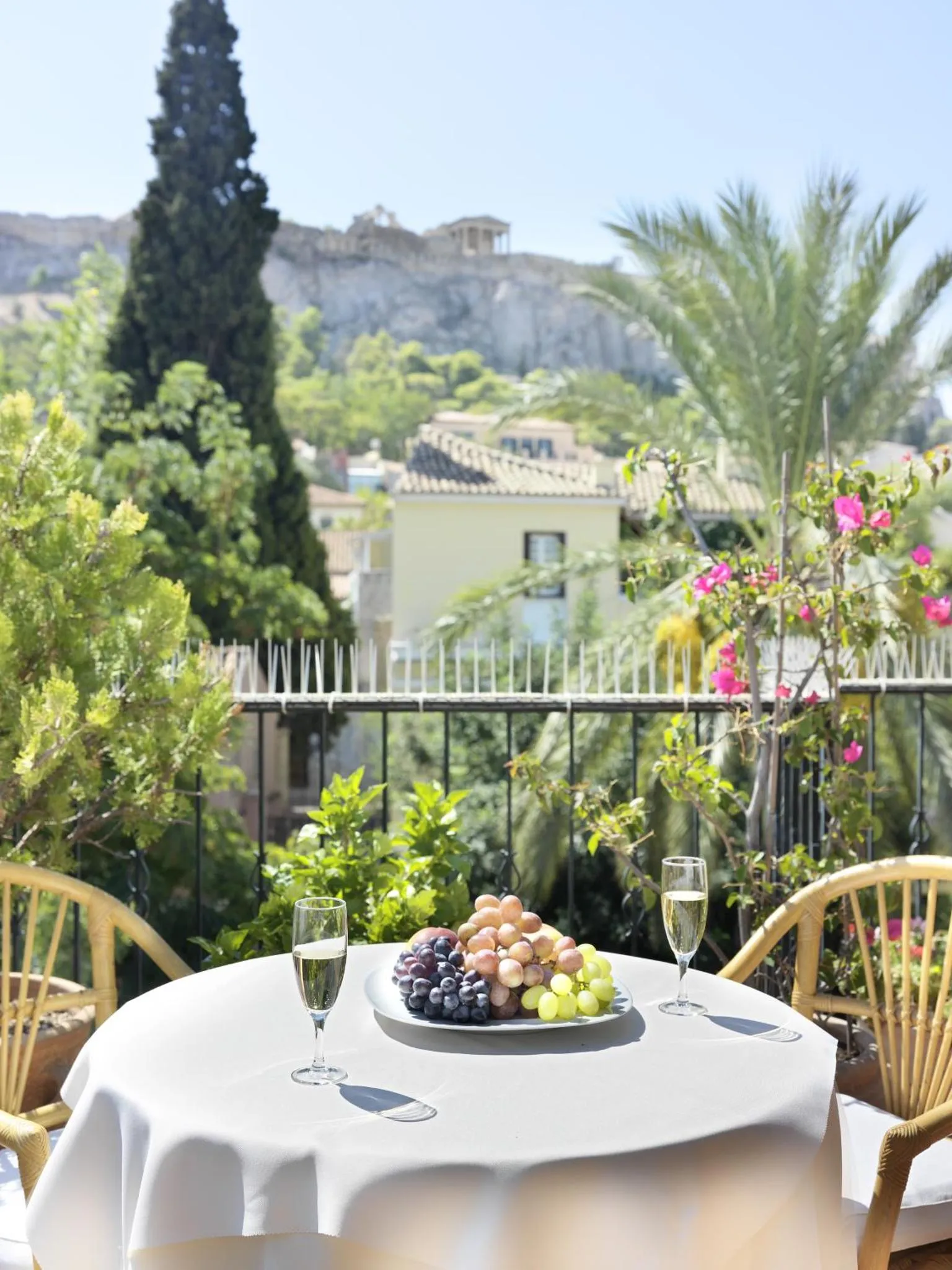 Une table avec des fruits et des verres de champagne est mise en scène sur une terrasse ensoleillée.