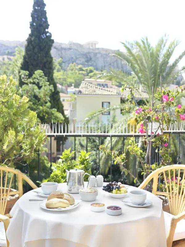 Une table mise avec des viennoiseries et des fruits est présentée sur une terrasse ensoleillée.