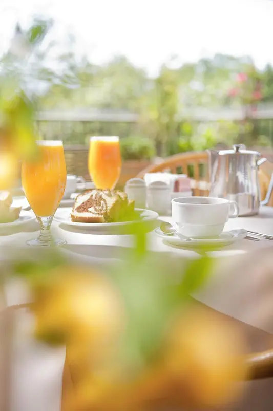 Une table est dressée avec des jus d'orange, une pâtisserie et une tasse de café.