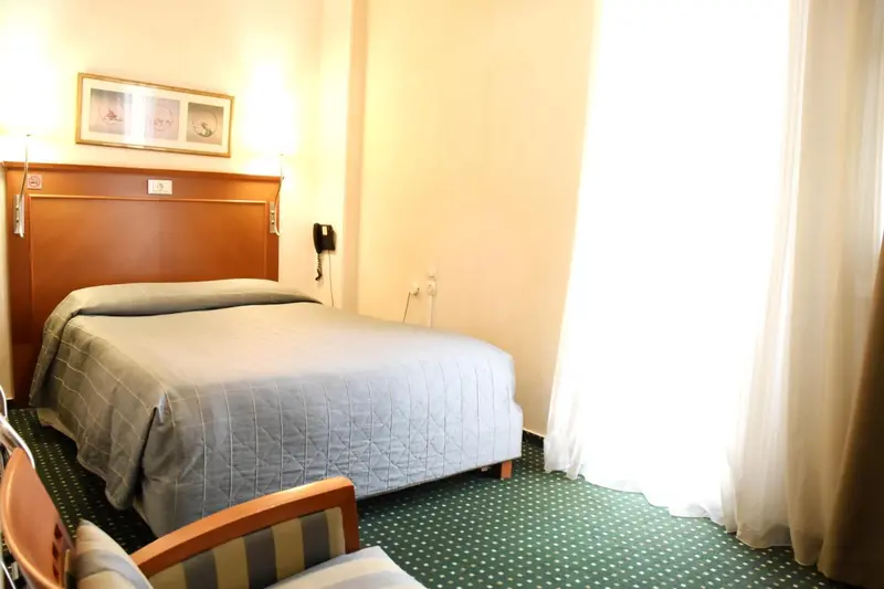 Une chambre lumineuse avec un lit recouvert d'une couverture et un fauteuil.