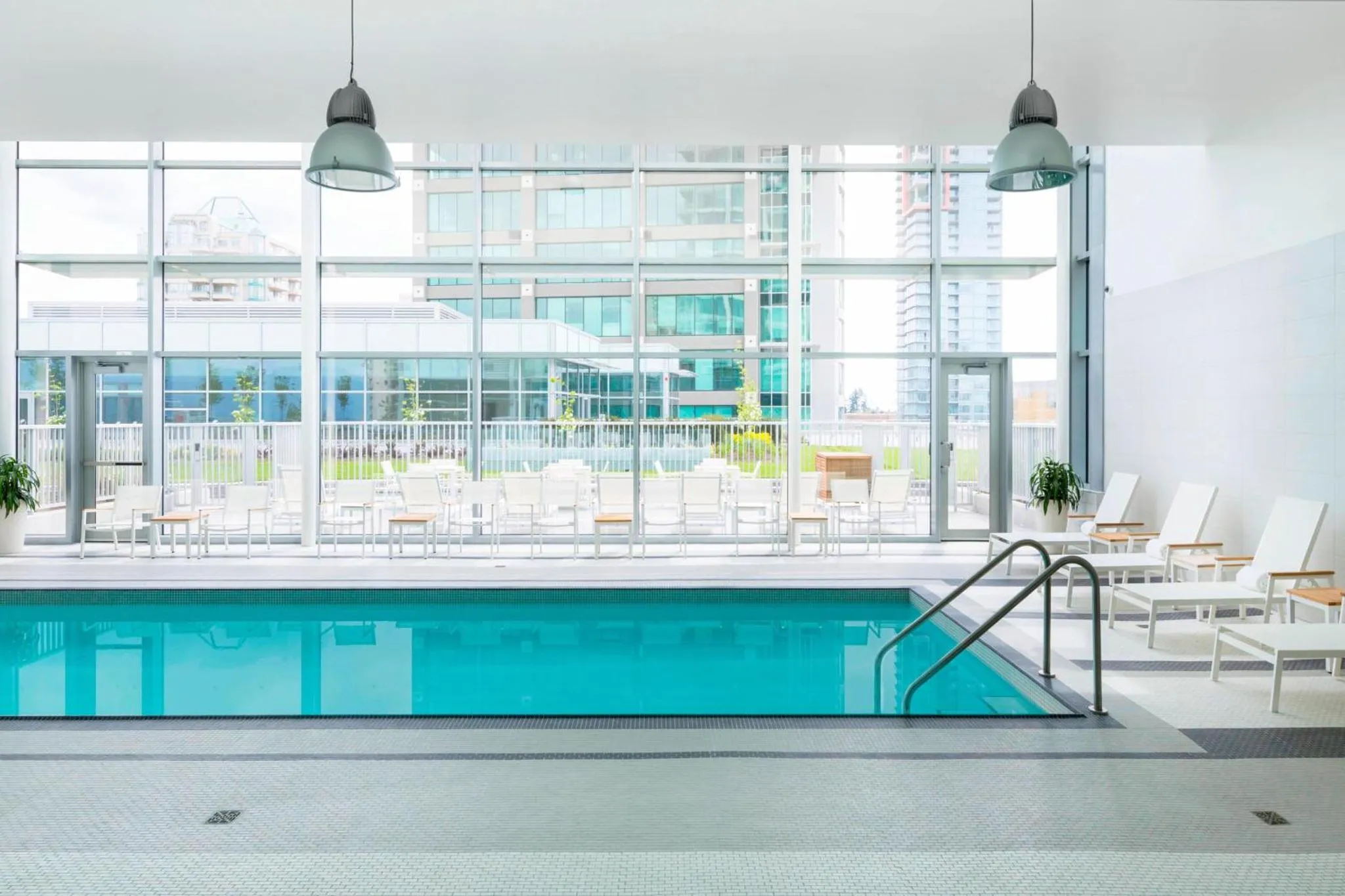 Une piscine interieure rectangulaire avec des transats blancs et des plantes vertes.