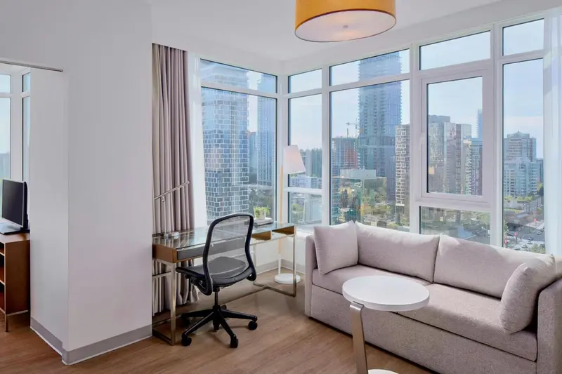 Espace de vie lumineux avec canapé et bureau près d'une grande fenêtre.