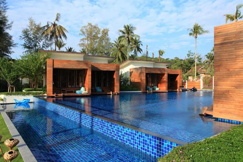 Une piscine rectangulaire bordée de bâtiments modernes en bois et de végétation tropicale.