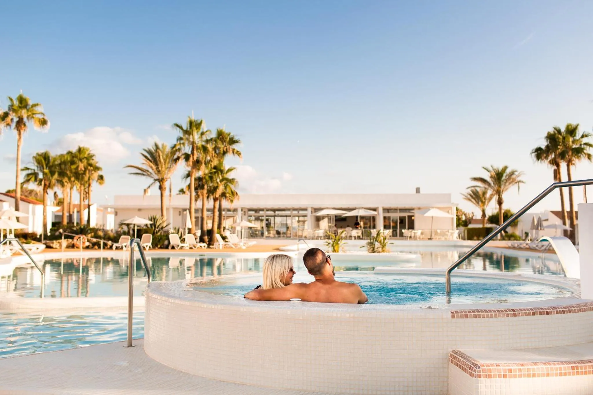 Un couple se détend dans un jacuzzi au bord d'une piscine ensoleillée.