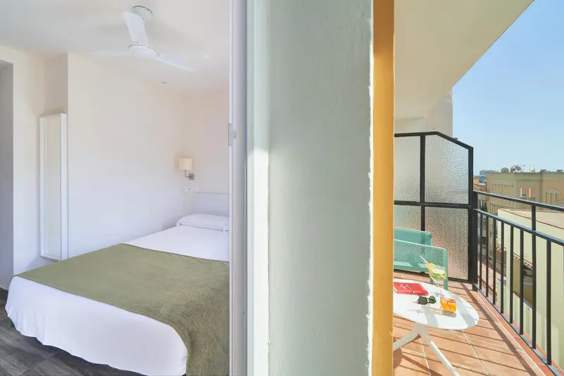 Une chambre lumineuse s'ouvre sur un balcon avec des sièges et une table.