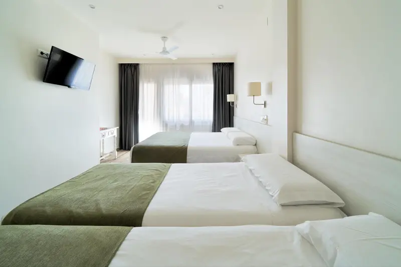 Une chambre lumineuse avec deux lits simples et une télévision murale.
