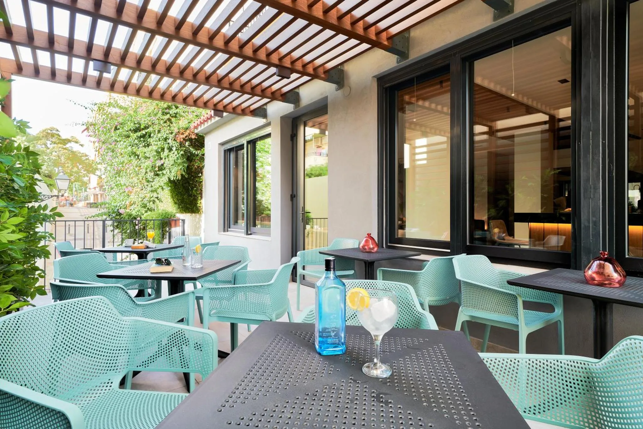 Terrasse ombragée avec tables et chaises turquoise.