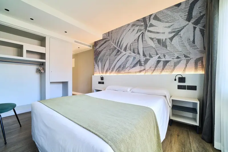 Une chambre lumineuse avec un grand lit et un mur décoré de motifs végétaux.
