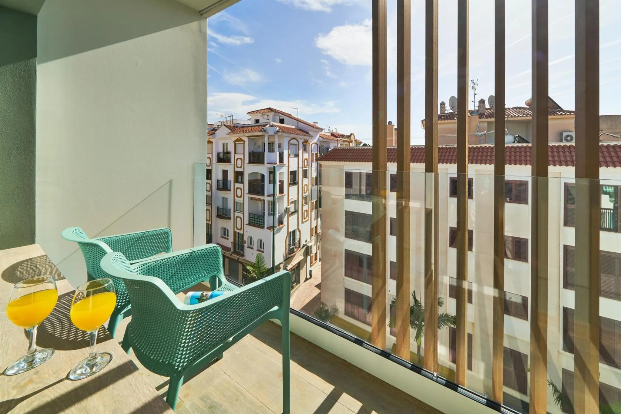 Deux fauteuils turquoise et une table basse avec des verres de jus d'orange sur une terrasse.