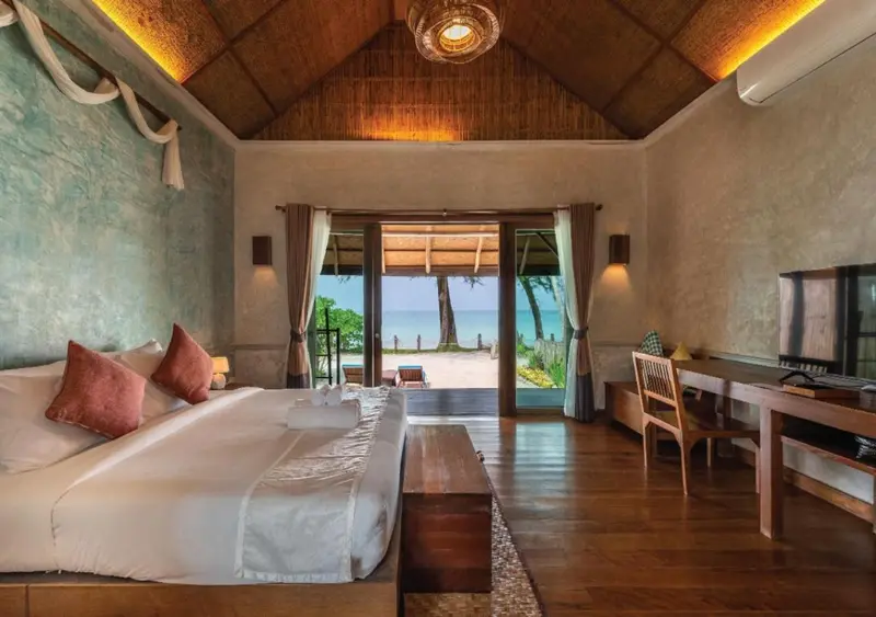 Une chambre lumineuse s'ouvre sur une vue de plage et de mer.