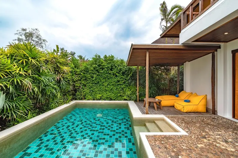 Petite piscine turquoise et mobilier d'extérieur jaune devant une maison blanche.