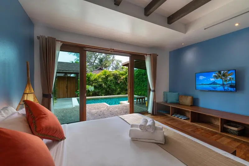 Une chambre lumineuse s'ouvre sur une piscine et une végétation luxuriante.