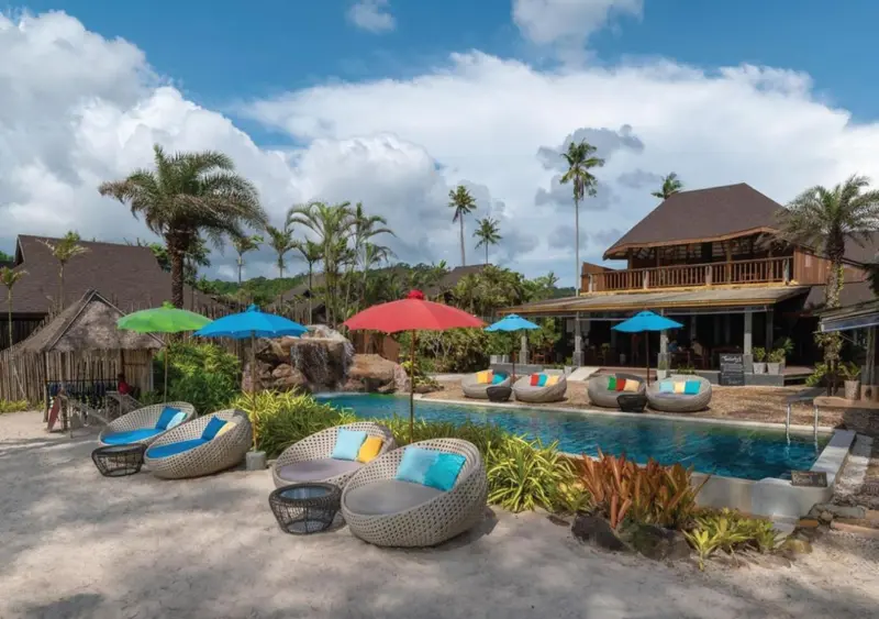 Transats et parasols colorés bordent une piscine au sein d'un complexe hôtelier tropical.