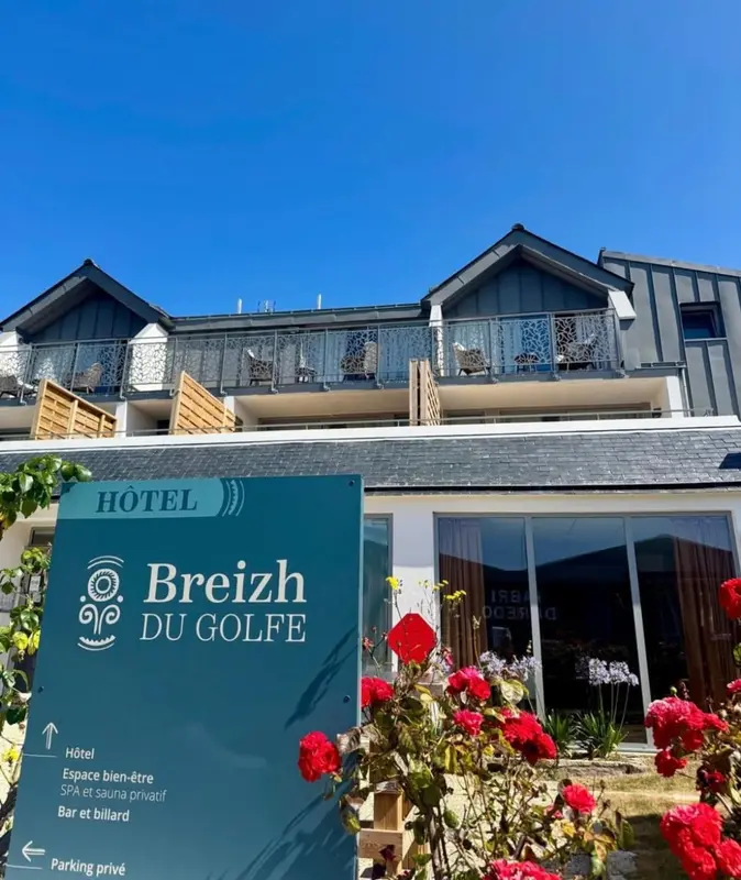 Façade d'un hôtel avec un jardin fleuri et une signalétique.