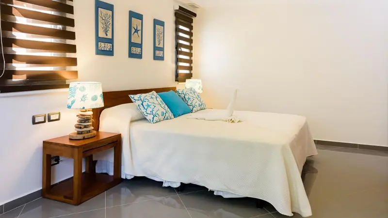 Une chambre lumineuse avec un grand lit recouvert d'une courtepointe blanche et de coussins bleus.