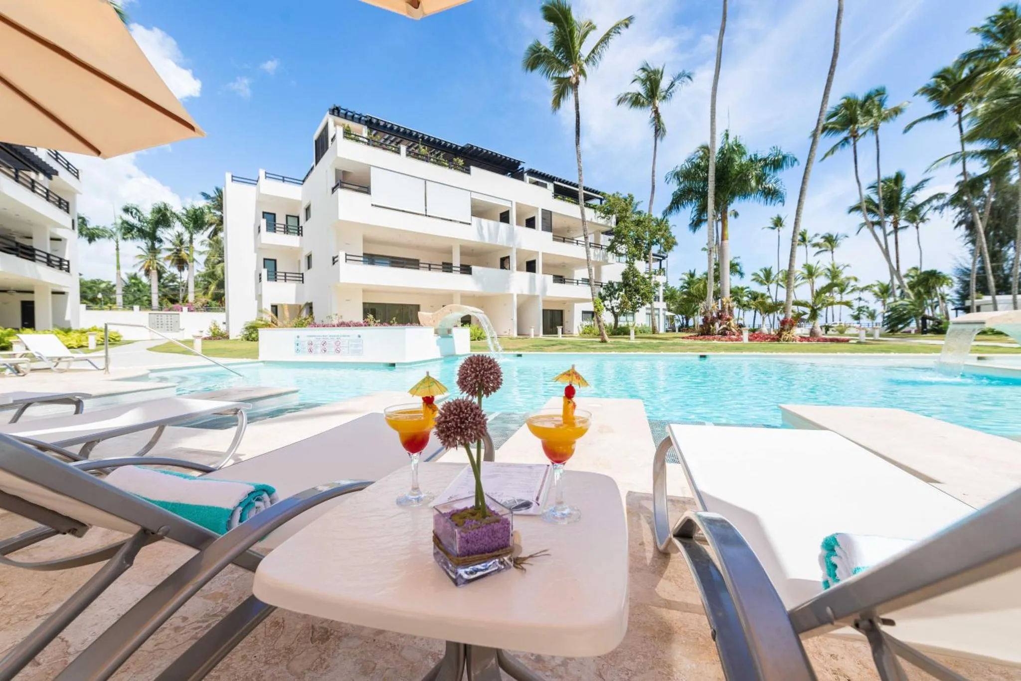 Deux cocktails colorés sur une table basse au bord d'une piscine ensoleillée.