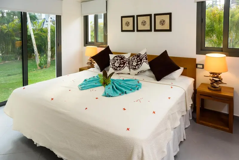 Une chambre lumineuse avec un grand lit recouvert d'une courtepointe blanche et de coussins décoratifs.