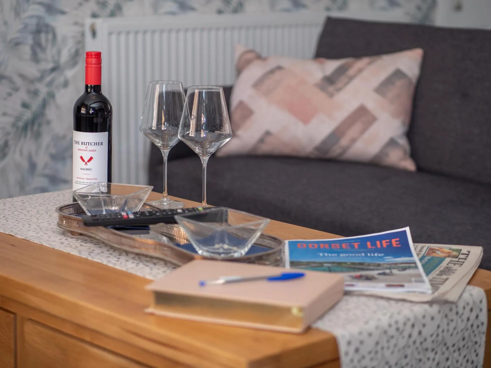 Une table basse avec une bouteille de vin, des verres et des magazines devant un canapé.