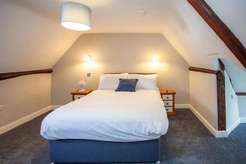 Une chambre lumineuse avec un grand lit recouvert d'une courtepointe blanche et de coussins bleus.