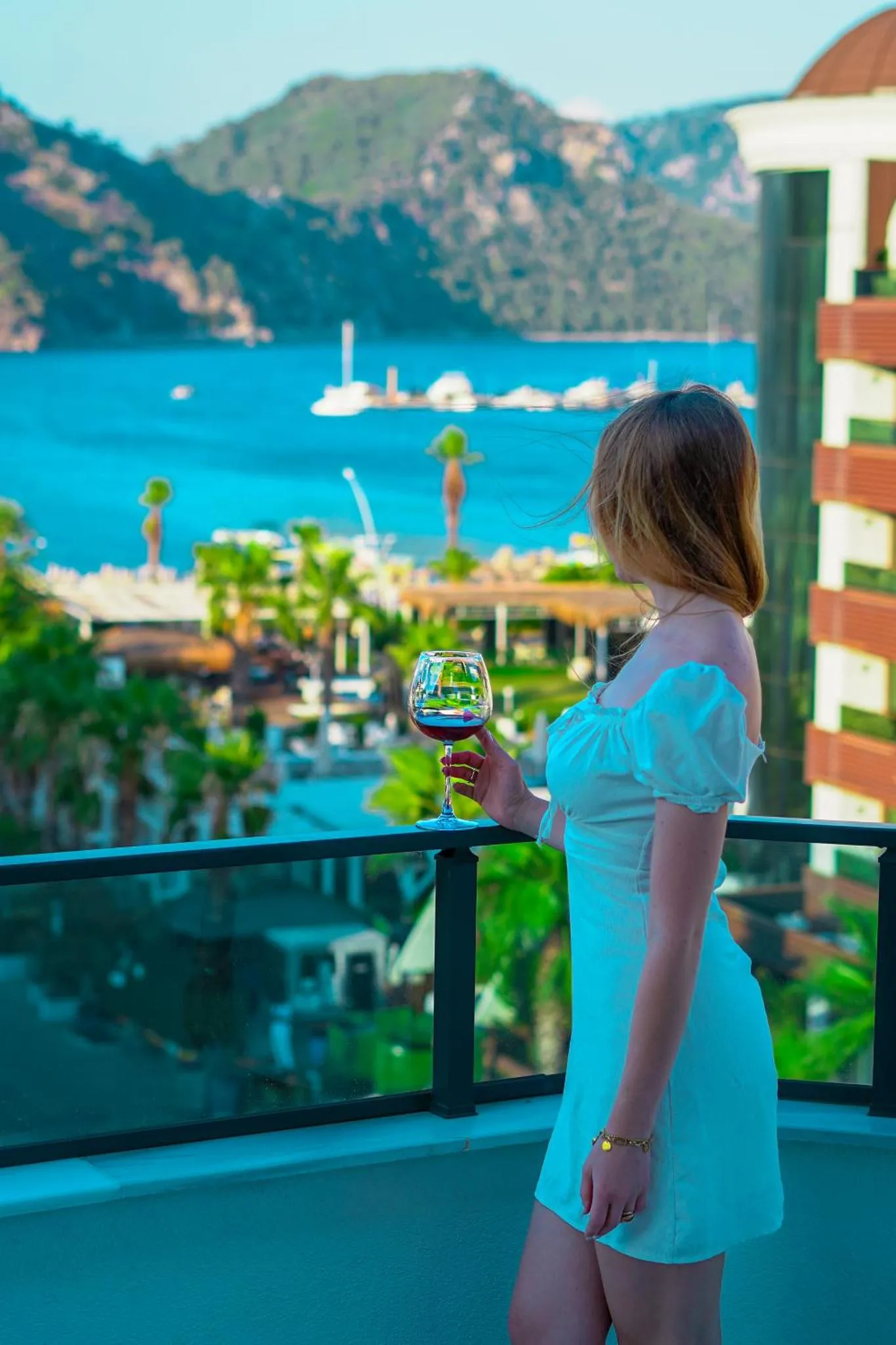Une femme tient un verre sur une terrasse avec vue sur la mer.