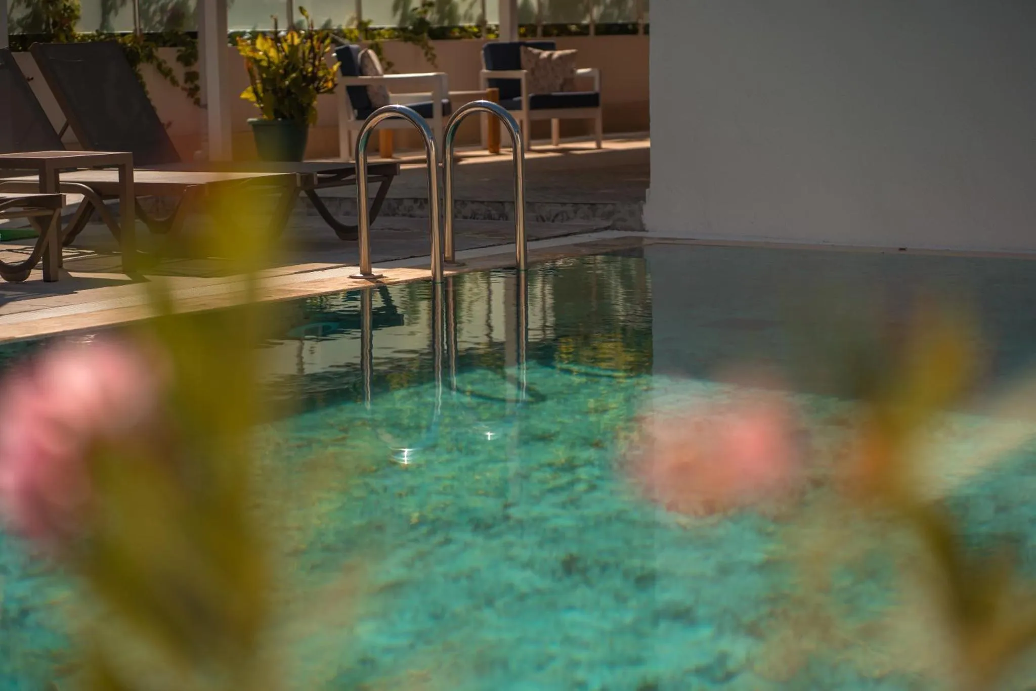 Une piscine turquoise avec des escaliers en acier inoxydable et des transats.
