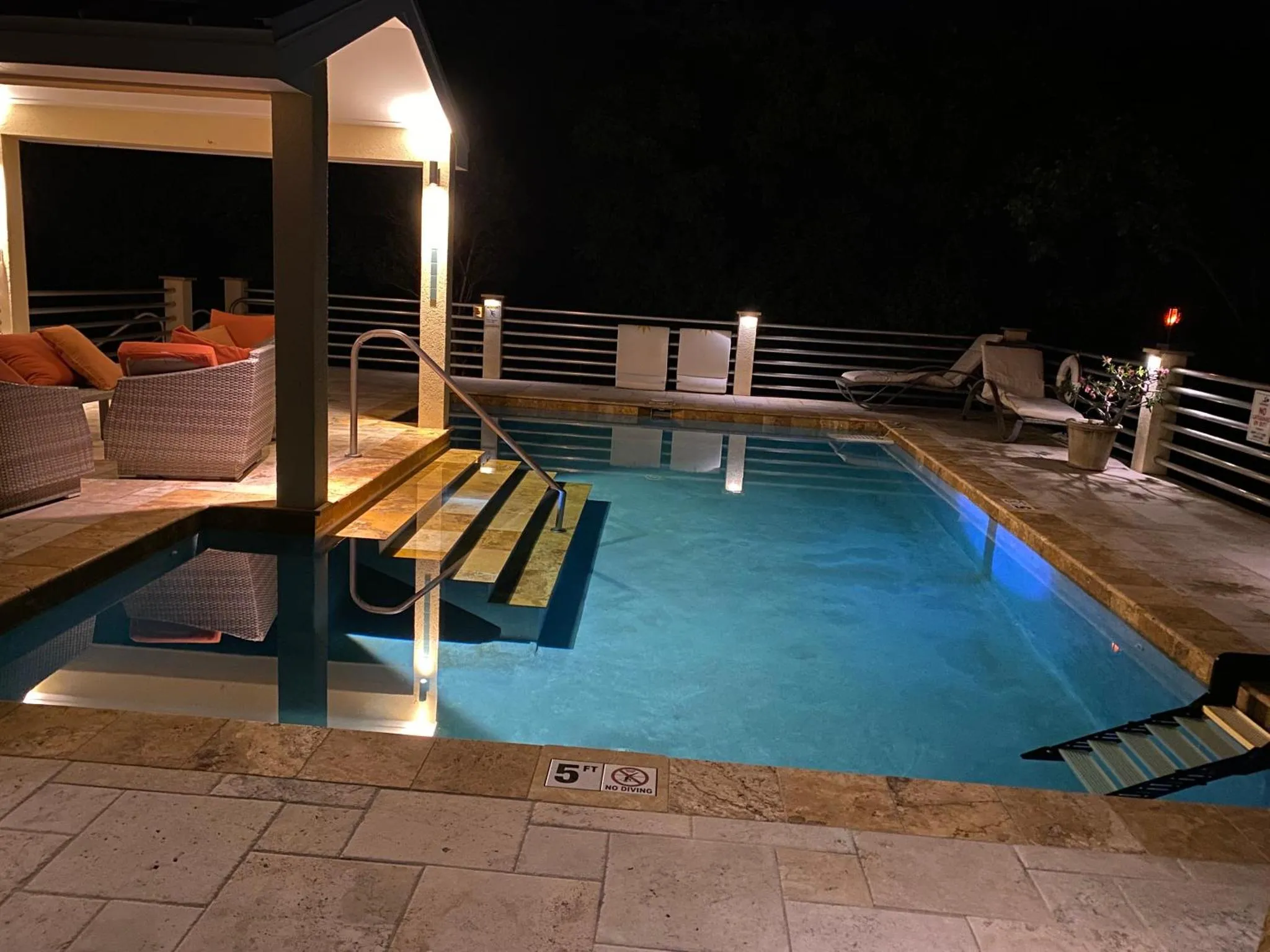 Une piscine éclairée avec des chaises longues et un escalier.