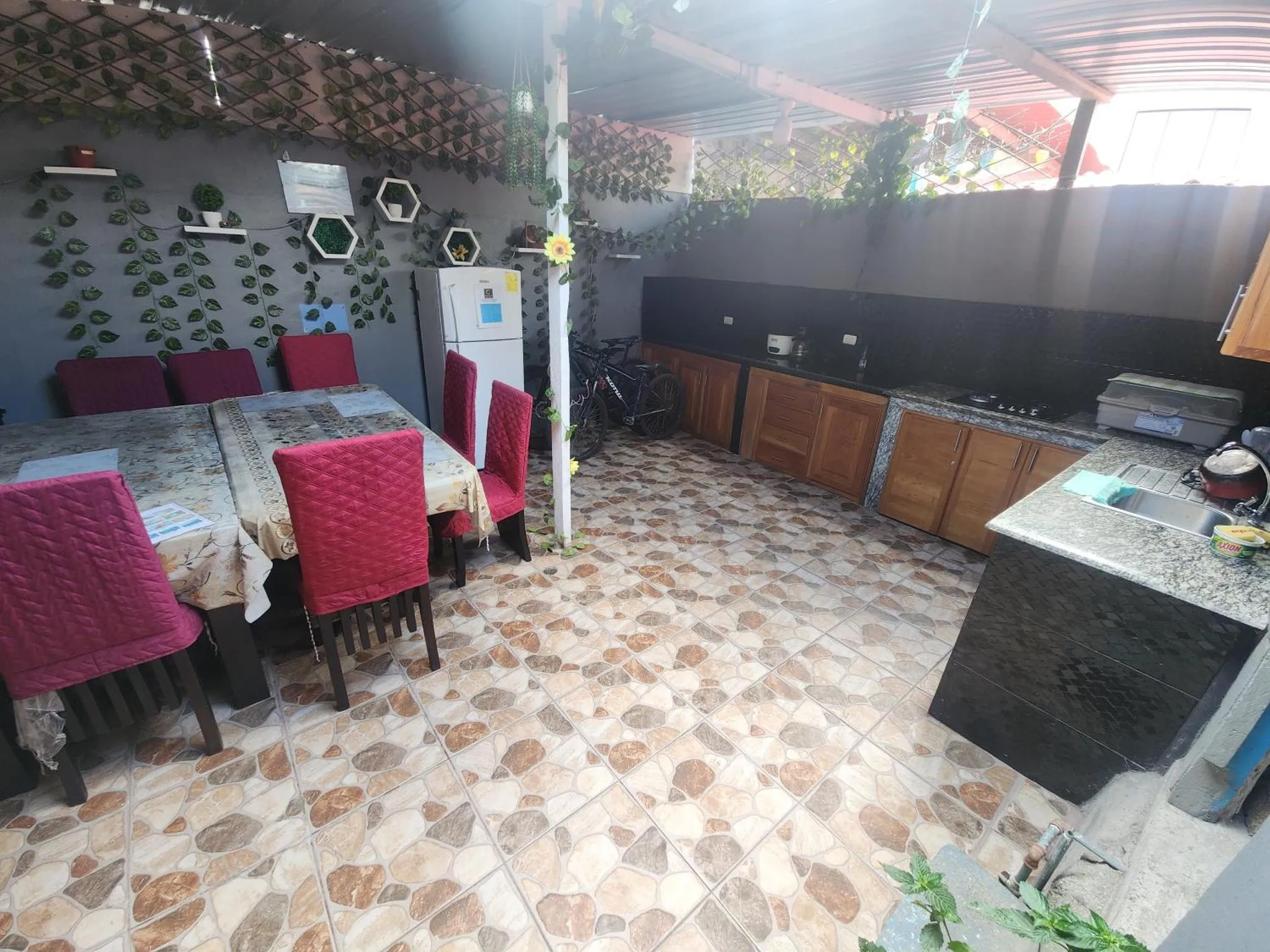 Une salle à manger extérieure avec des tables et des chaises rouges, et une cuisine équipée.