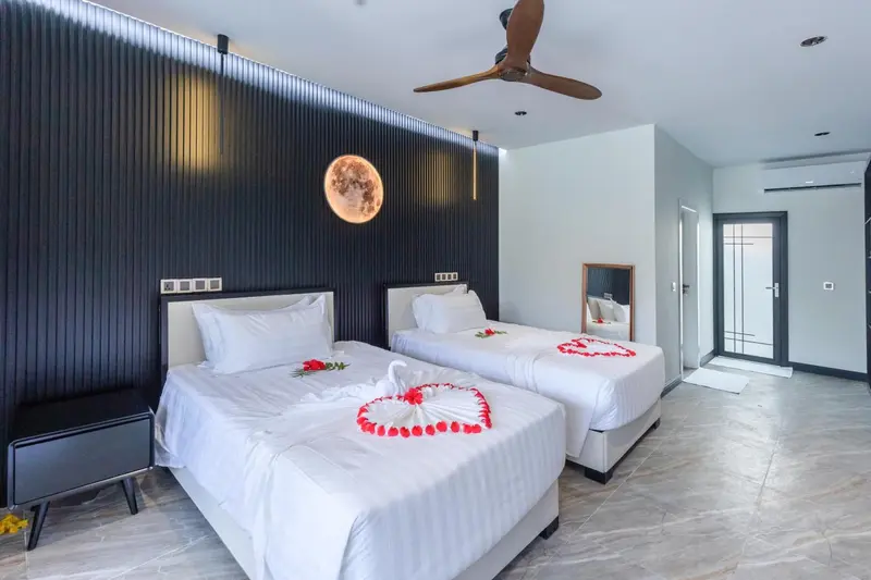 Chambre lumineuse avec deux lits décorés de fleurs et d'une télévision murale.