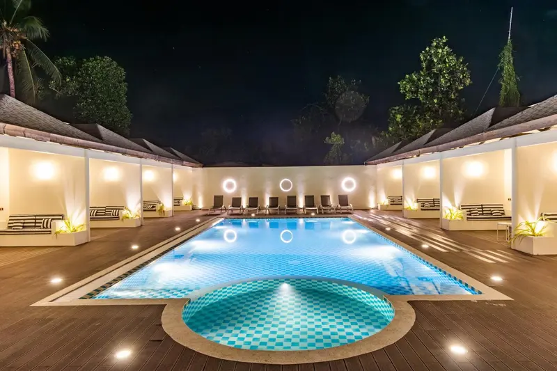 Piscine illuminée devant des bâtiments éclairés la nuit.