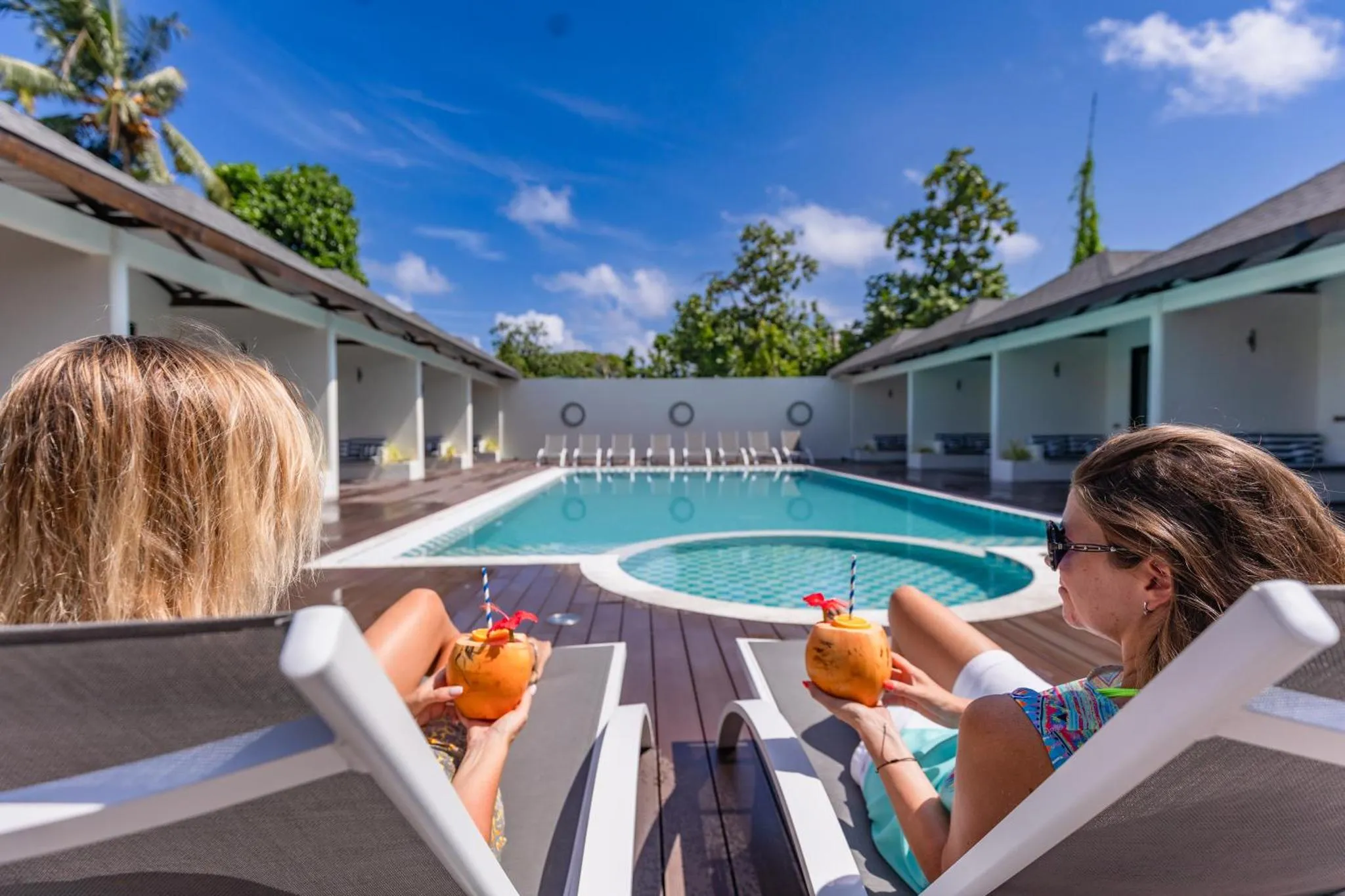 Deux personnes se détendent sur des transats au bord d'une piscine turquoise.