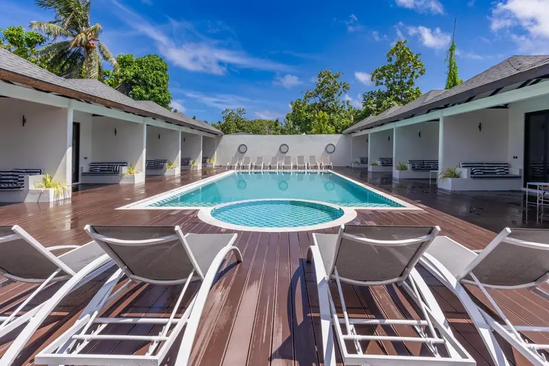 Transats blancs disposés devant une piscine rectangulaire entourée d'une terrasse en bois.