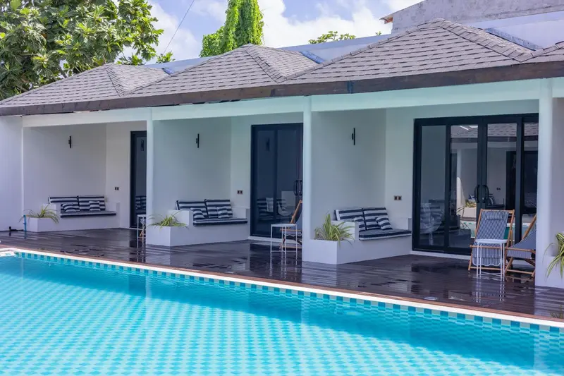 Terrasse avec transats devant des logements blancs et une piscine.
