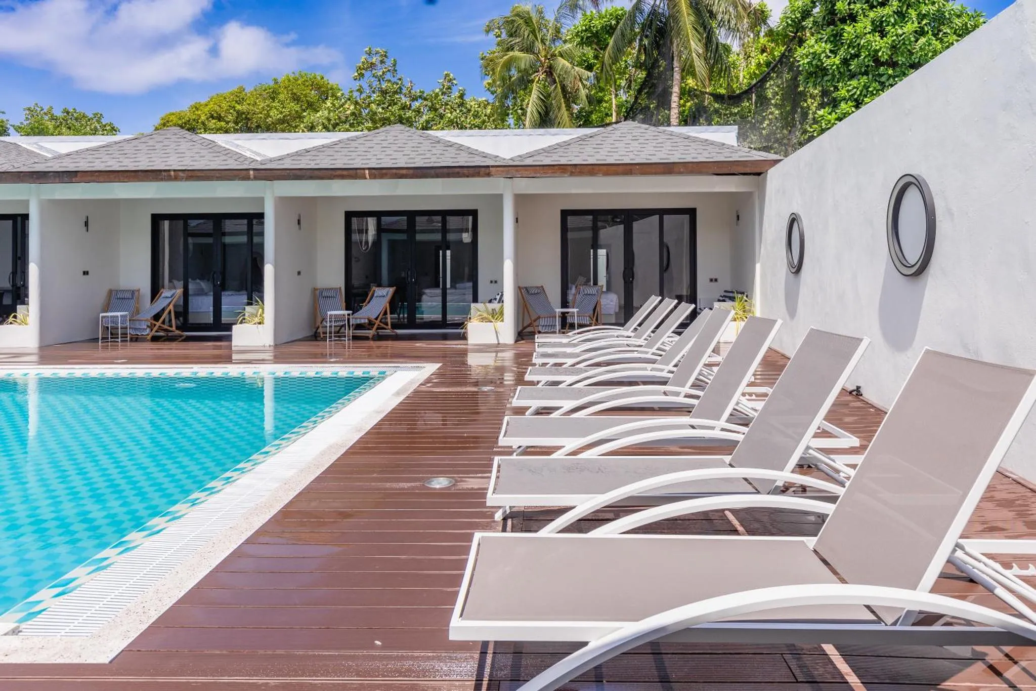 Transats alignés au bord d'une piscine turquoise dans un cadre tropical.