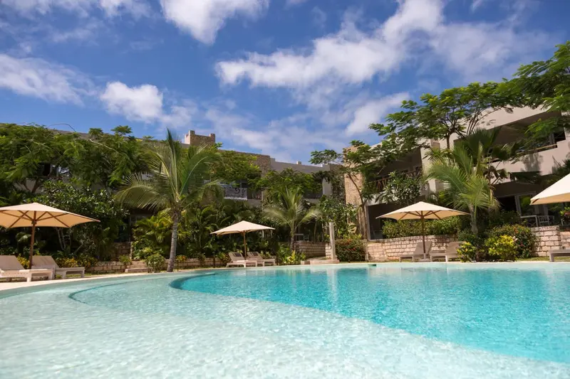 Piscine turquoise bordée de chaises longues et de parasols, dans un cadre tropical luxuriant.