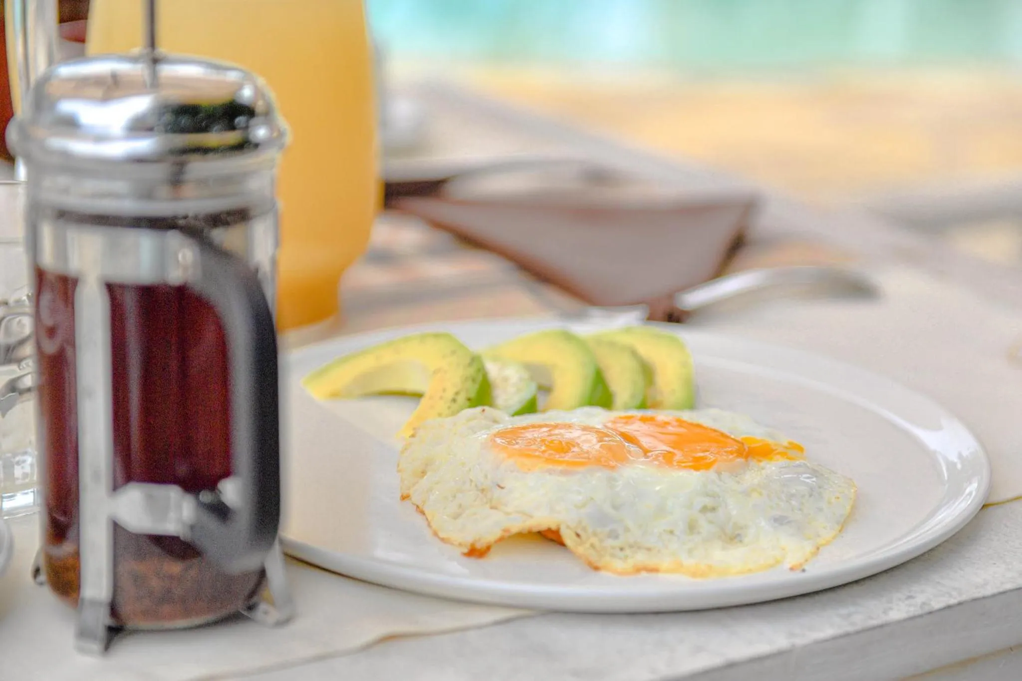 Un petit-déjeuner avec un œuf au plat, de l'avocat et une cafetière à piston.