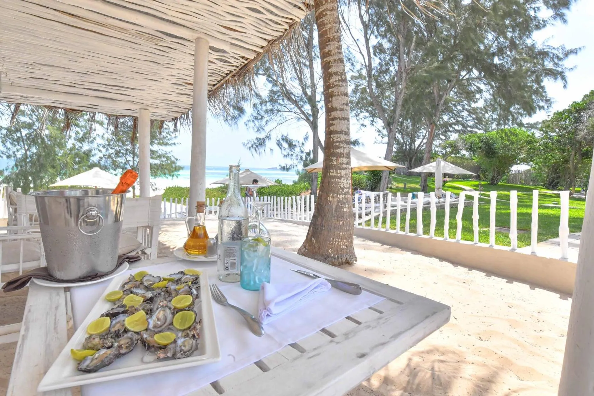 Une table dressée avec des huîtres et des boissons sur une terrasse ensoleillée face à la mer.