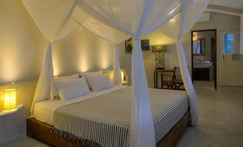 Une chambre lumineuse avec un grand lit à baldaquin et une décoration sobre.