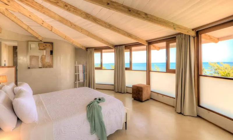 Une chambre lumineuse avec un lit recouvert de draps blancs et une vue sur la mer.