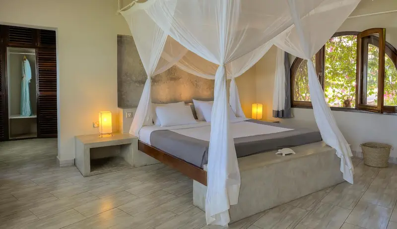 Une chambre lumineuse avec un grand lit à baldaquin et une fenêtre ouverte sur la végétation.