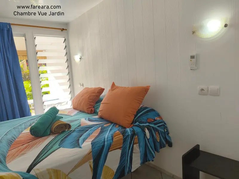 Une chambre lumineuse avec un lit recouvert d'une courtepointe aux motifs tropicaux et des oreillers colorés.
