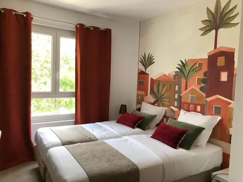 Chambre lumineuse avec deux lits simples et une décoration murale colorée.