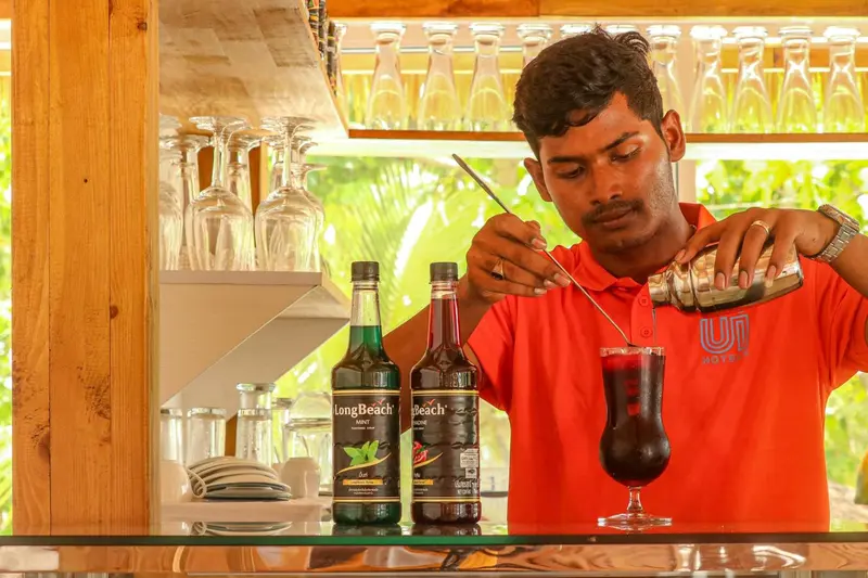 Un barman prépare un cocktail derrière un comptoir en bois.