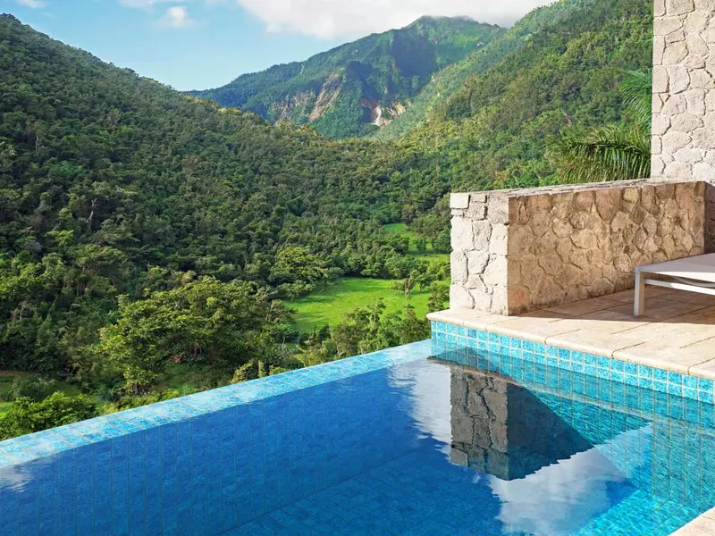 Une piscine à débordement offre une vue panoramique sur une vallée verdoyante et des montagnes.